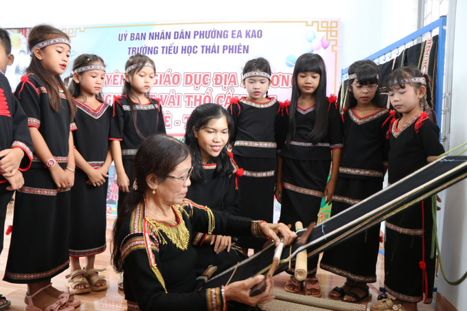 Nghệ nhân H’Đer Buôn Krông (buôn H’Đơk, phường Ea Kao, tỉnh Đắk Lắk), người có hơn 20 năm gắn bó với nghề dệt, hướng dẫn cho học sinh tìm hiểu về cách dệt vải thổ cẩm.