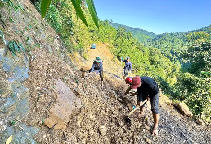 Người dân dùng cuốc, xẻng và các dụng cụ thủ công phá, san gạt đất đá sạt lở tại các dốc Co Pọng, Co Ngóa và Co Phác Pặp trên tuyến đường từ Na Ngân ra trung tâm xã Nga My. Ảnh: TTXVN phát