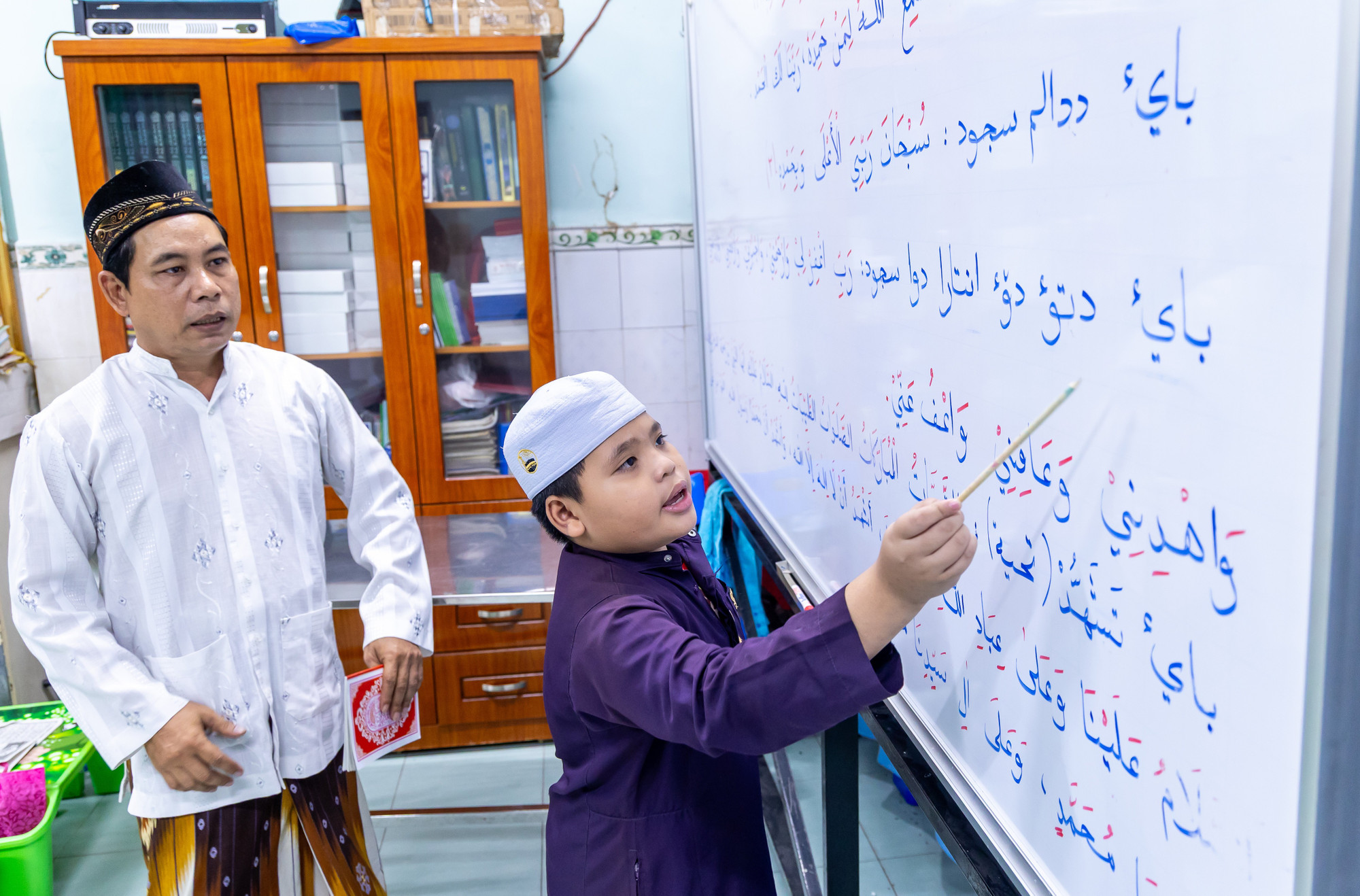 Thầy Muhammad Osry hỗ trợ các em học sinh đọc chữ Chăm lớp học ở Thánh đường Jamiul Anwar, phường Chánh Hưng. lophoctiengcham8.jpg