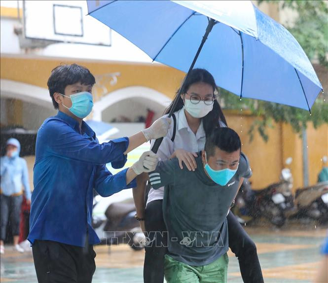 Thí sinh bị đau chân được phụ huynh và tình nguyện giúp đỡ tới điểm thi trường THPT Trần Nhân Tông. Ảnh: Thanh Tùng - TTXVN Kỳ thi tuyển sinh lớp 10 tại Hà Nội: Đoàn kết làm nên thành công của Kỳ thi “đặc biệt” ảnh 1