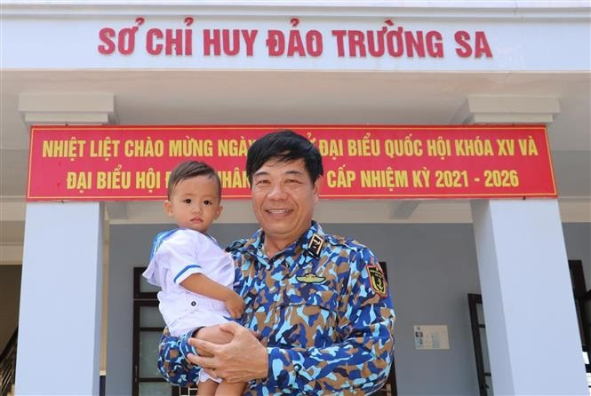 Chuẩn Đô đốc Hải quân nhân dân Việt Nam Phan Tuấn Hùng và bé Lâm Nhật Kiến Huy (18 tháng tuổi, công dân thị trấn Trường Sa) trước Sở chỉ huy đảo Trường Sa. Ảnh: TTXVN Huyện đảo Trường Sa hướng tới "Ngày hội non sông" ảnh 3