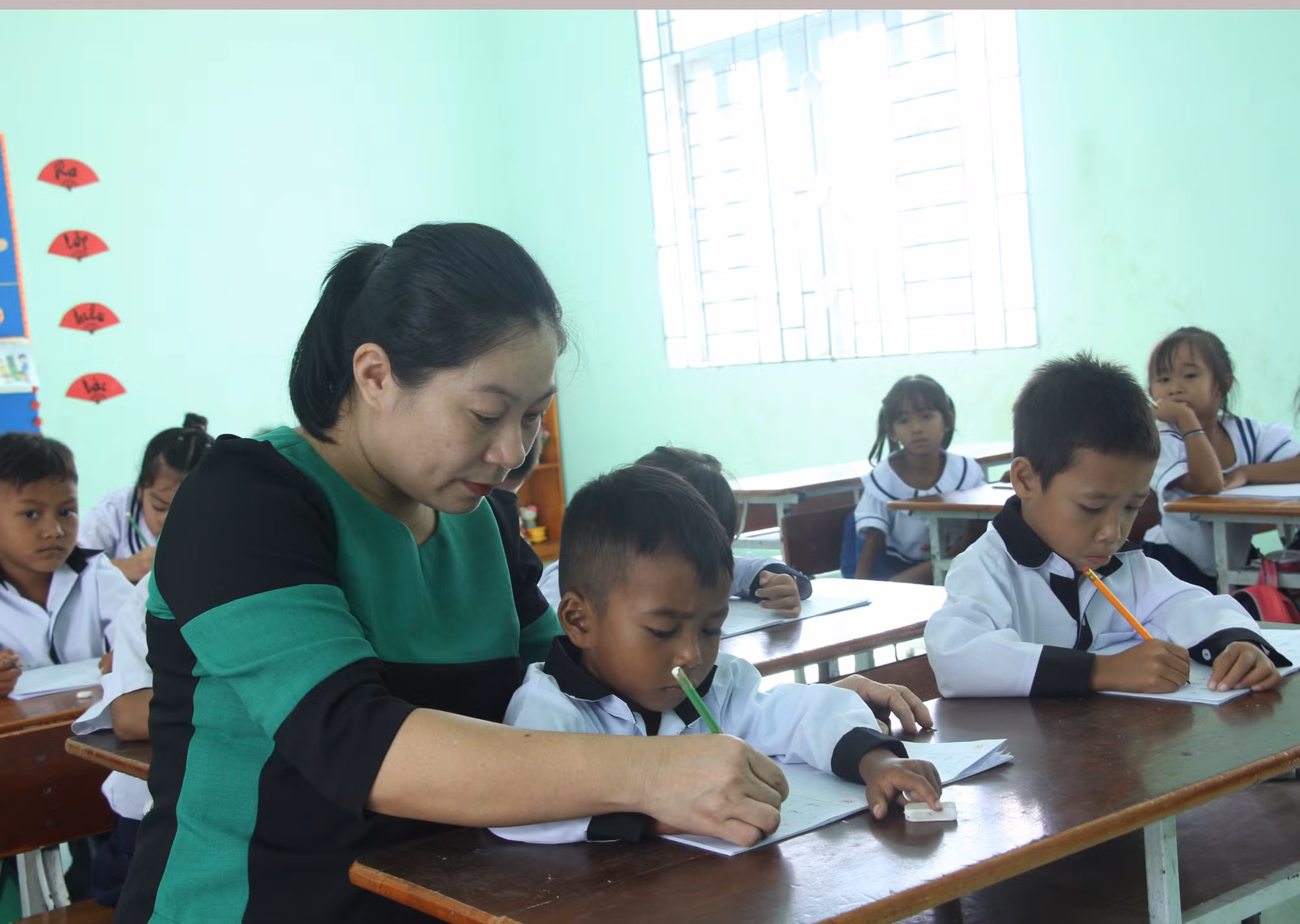 Cô Bùi Thị Hương, Trường Tiểu học Phước Thắng, xã Bác Ái, tỉnh Khánh Hòa cầm bút và tay của trẻ để hướng dẫn trẻ cách tập viết chữ tiếng Việt.