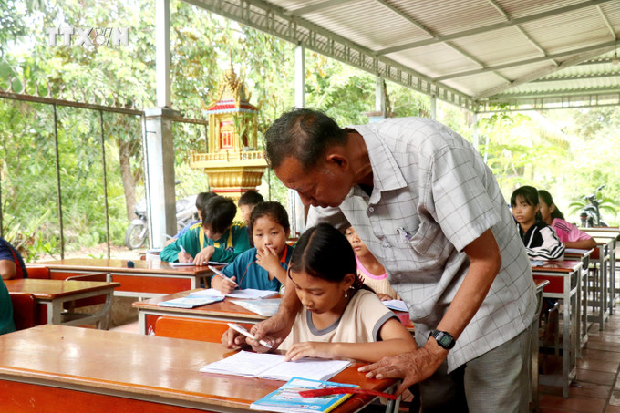 Ông Thạch Hoàng Anh kiểm tra chữ viết của học trò tại lớp dạy chữ Khmer ấp Thới Trường 2, xã Thới Xuân. Ảnh: Thu Hiền - TTXVN vna_potal_van_hoa_soi_duong_truyen_giu_chu_khmer_cho_the_he_sau_7484513.jpg