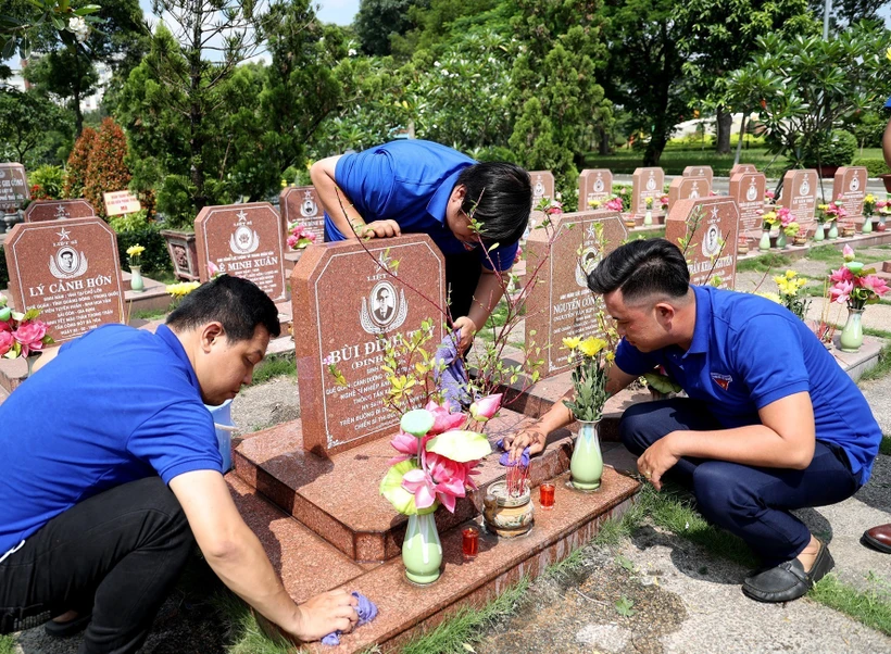 Đoàn viên Cơ quan TTXVN khu vực phía Nam chăm sóc phần mộ Anh hùng liệt sĩ - nhà báo Bùi Đình Túy, nguyên Phó Giám đốc Thông tấn xã Giải phóng. Ảnh: Hồng Đạt - TTXVN