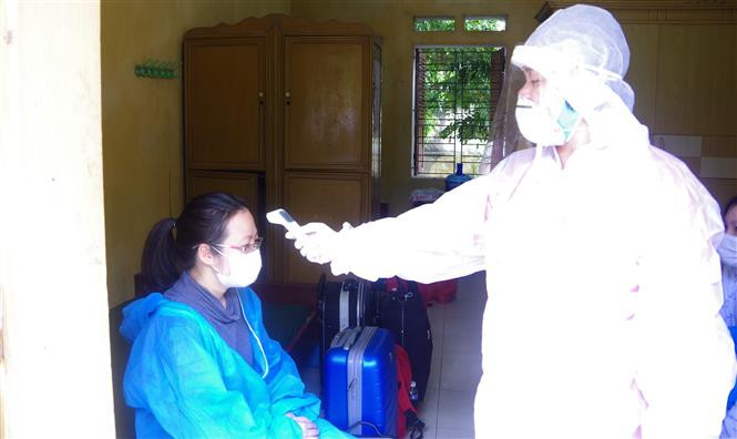 Cán bộ y tế kiểm tra thân nhiệt cho công dân làm thủ tục cách ly tập trung. Ảnh: Đinh Tuấn-TTXVN 