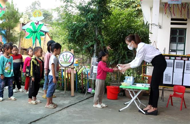 Các học sinh mầm non được cô giáo đo thân nhiệt, rửa tay sát khuẩn trước khi vào lớp học. Ảnh: Quốc Khánh - TTXVN 