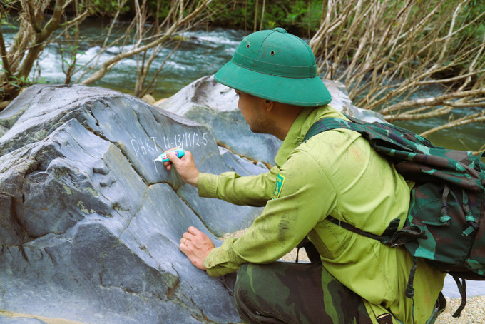 Lực lượng kiểm lâm Trạm quản lý, bảo vệ rừng Bình Chuẩn đánh dấu vị trí lên tảng đá bên thượng nguồn khe Cố trong hành trình di chuyển để “làm mốc dấu” cho lần di chuyển khác khi vào thu hồi máy bẫy ảnh. Ảnh: Xuân Tiến/TTXVN