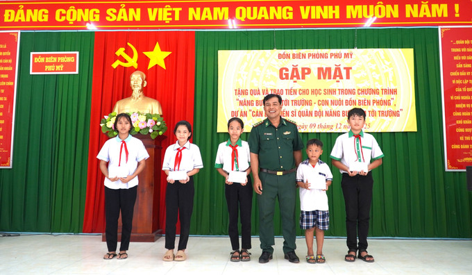 Thượng tá Danh Kim Huôl, Chính trị viên Đồn Biên phòng Phú Mỹ trao quà cho các học sinh thuộc chương trình “Nâng bước em tới trường - Con nuôi Đồn Biên phòng”.