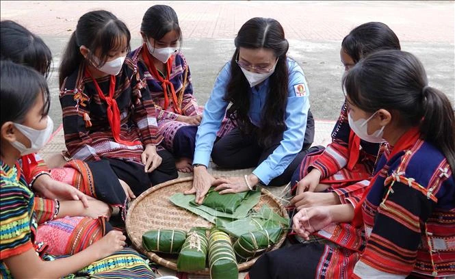 Bí thư Trung ương Đoàn, Chủ tịch Hội đồng đội Trung ương Nguyễn Phạm Duy Trang hướng dẫn các em học sinh Trường Phổ thông dân tộc nội trú THCS và THPT Vân Canh gói bánh chưng. Ảnh: Phạm Kha – TTXVN