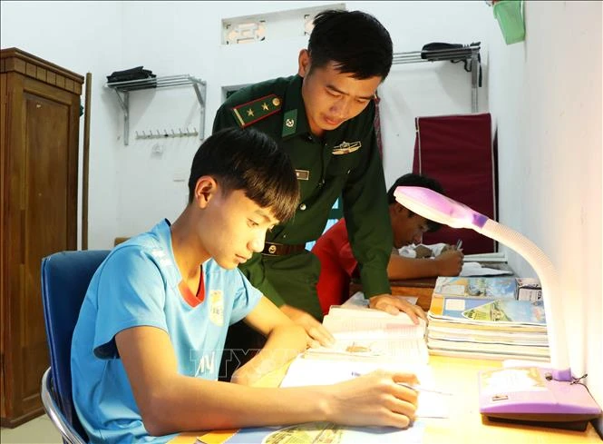 Trung úy Dì A De, Đội trưởng Đội Ma túy Đồn Biên phòng Thu Lũm dạy học cho cháu Mạ Đức Mạnh. Ảnh: Hoàng Thùy Oanh – TTXVN