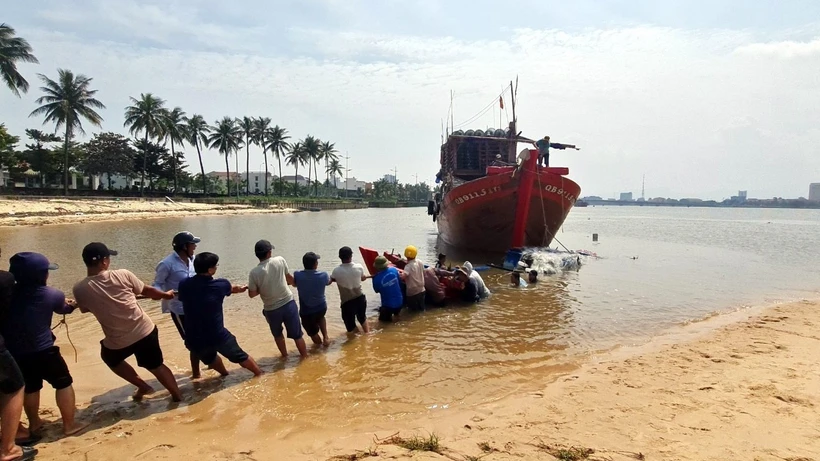 Người dân địa phương hỗ trợ lai dắt và trục vớt thuyền bị chìm của ngư dân đưa vào bờ. Ảnh: TTXVN phát