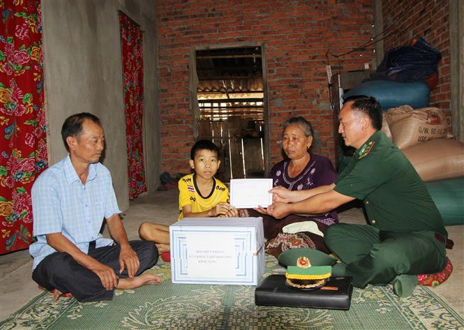 Cán bộ Đồn Biên phòng Cửa khẩu Chiềng Khương, Bộ Chỉ huy Bộ đội Biên phòng tỉnh Sơn La thăm hỏi, động viên và trao tiền hỗ trợ cho gia đình cháu Thạo Phe ở bản Đán, huyện Mường Ét, tỉnh Hủa Phăn (Lào) có hoàn cảnh đặc biệt khó khăn mà đơn vị đỡ đầu. Ảnh: Nguyễn Cường - TTXVN. 60 năm quan hệ Việt Nam - Lào: Thắm tình hữu nghị bên dòng sông Mã ảnh 3