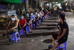 Các tiểu thương ngồi xếp hàng đảm bảo giãn khoảng cách chờ lấy mẫu xét nghiệm trong đêm. Ảnh: Thành Đạt - TTXVN 
