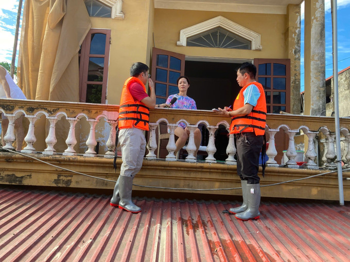 Phóng viên TTXVN đứng trên mái nhà phỏng vấn người dân về tình hình ứng phó với ngập lụt. Ảnh: Thắng Trung/TTXVN bao-81025.jpg